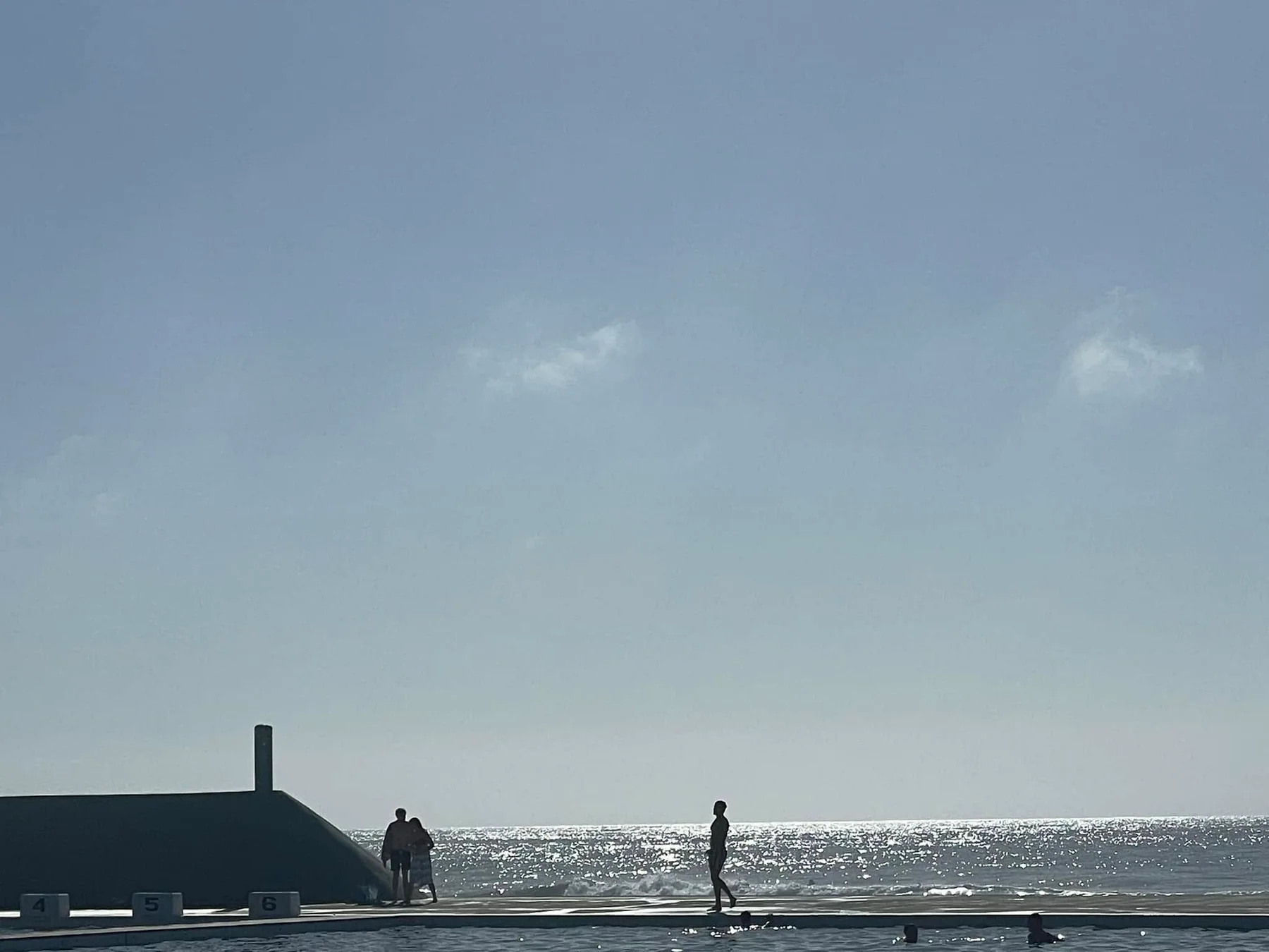 Silhouetted figures at a bright seafront pool